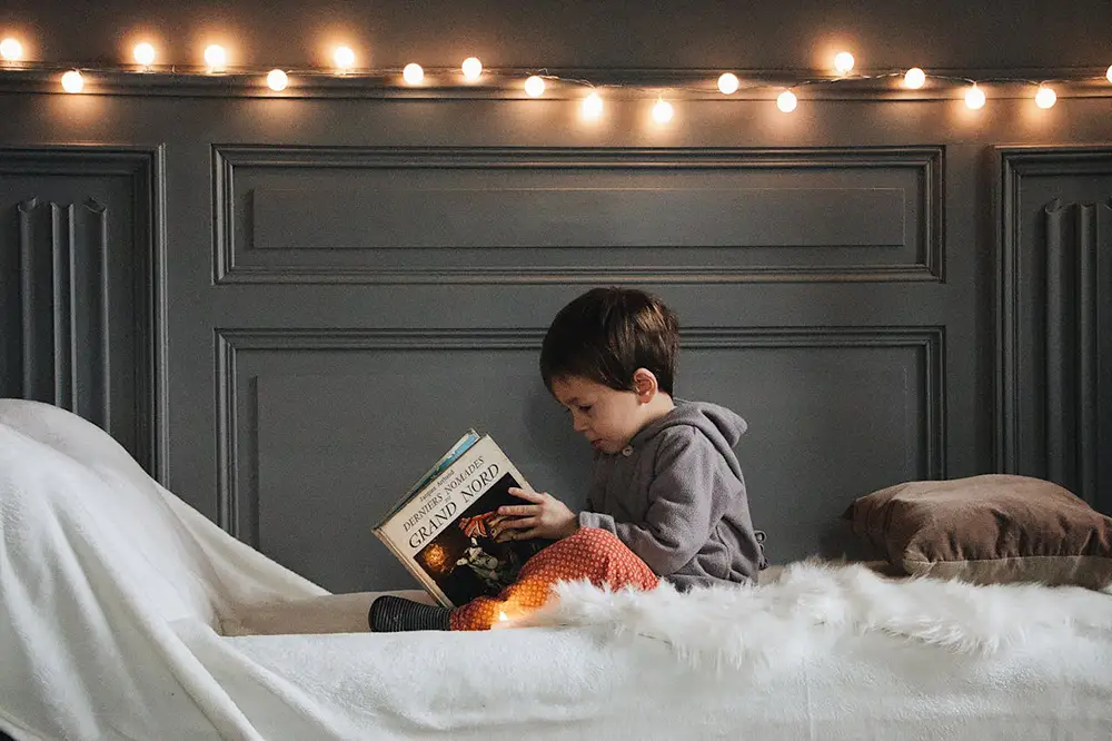 enfant assis sur un lit , regardant un livre dans sa chambre