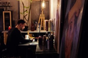 Artiste installé à sa table dans un atelier chaleureux, entouré de chevalets et de toiles peintes